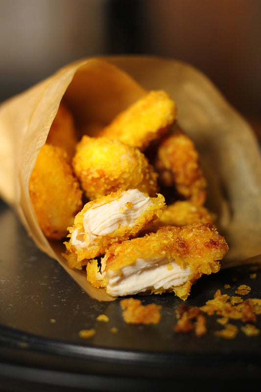 Fried chicken nuggets spill out of a brown paper wrapper.