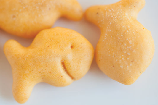 Three yellow goldfish crackers up close. One of them looks like it is smiling at the camera.