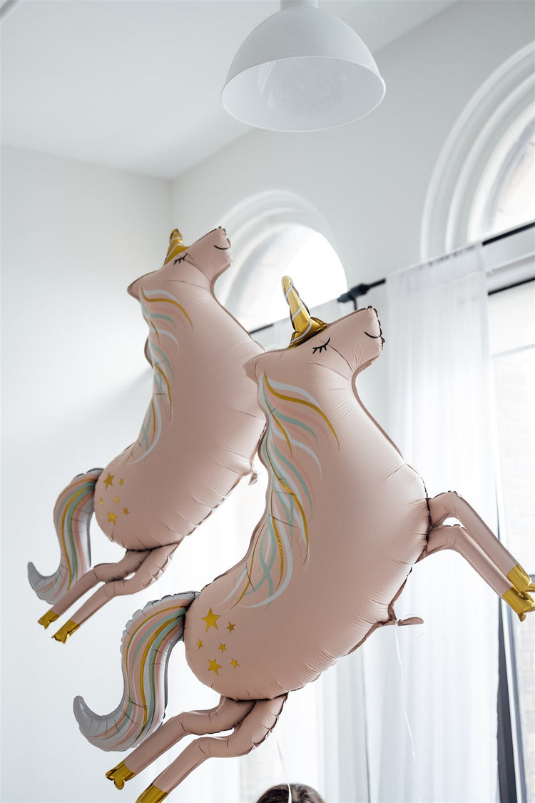 Two pink unicorn foil balloons in a white room.