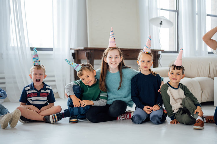 Happy kids sitting together, wearing unicorn horn party hats.