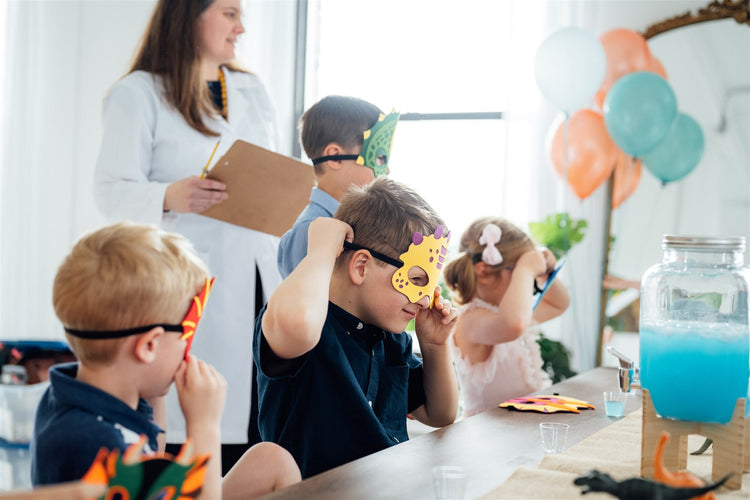 Children at a birthday party putting on dinosaur masks.